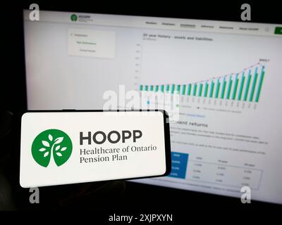 Stuttgart, Allemagne, 10-16-2023 : personne tenant un téléphone portable avec le logo du régime de pensions de santé de l'Ontario (HOOPP) devant la page Web de l'entreprise. Banque D'Images
