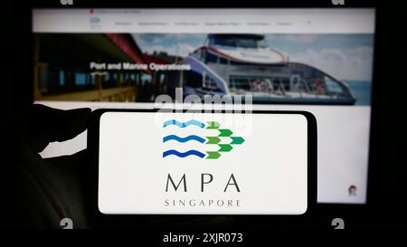 Stuttgart, Allemagne, 11-06-2023 : personne tenant un téléphone portable avec le logo de l'Autorité maritime et portuaire de Singapour (MPA) devant la page Web. Mise au point Banque D'Images