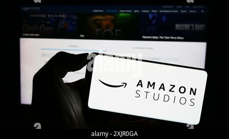 Stuttgart, Allemagne, 11-08-2023 : personne tenant un téléphone portable avec le logo de la société américaine de production cinématographique et télévisuelle Amazon Studios devant le web Banque D'Images