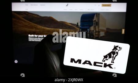 Stuttgart, Allemagne, 11-10-2023 : personne tenant un téléphone portable avec le logo de la société américaine de fabrication de camions Mack Trucks Inc en face de la page Web de l'entreprise. Banque D'Images