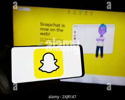 Stuttgart, Allemagne, 11-14-2023 : personne tenant un téléphone portable avec le logo de l'application de messagerie instantanée multimédia américaine Snapchat en face de la page Web de l'entreprise. Mise au point Banque D'Images