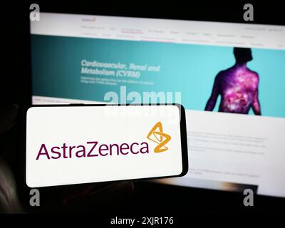 Stuttgart, Allemagne, 11-16-2023 : personne tenant un téléphone portable avec le logo de la société pharmaceutique AstraZeneca plc devant la page Web de l'entreprise. Concentrez-vous sur Banque D'Images