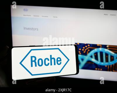 Stuttgart, Allemagne, 11-16-2023 : personne tenant un smartphone avec le logo de la société suisse de soins de santé Roche Holding AG devant le site. Concentrez-vous sur le téléphone Banque D'Images