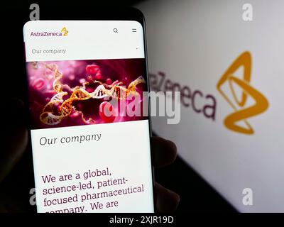 Stuttgart, Allemagne, 11-16-2023 : personne tenant un téléphone portable avec la page Web de la société pharmaceutique AstraZeneca plc devant le logo de l'entreprise. Concentrez-vous sur Banque D'Images