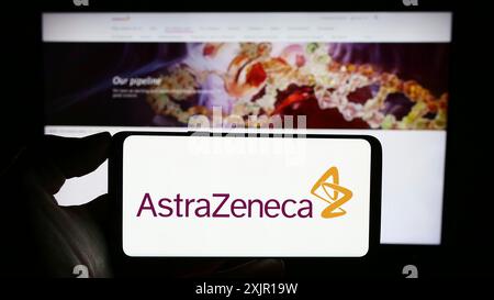 Stuttgart, Allemagne, 11-16-2023 : personne tenant un téléphone portable avec le logo de la société pharmaceutique AstraZeneca plc devant la page Web de l'entreprise. Mise au point Banque D'Images