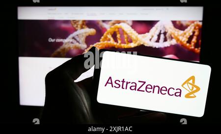 Stuttgart, Allemagne, 11-16-2023 : personne tenant un smartphone avec le logo de la société pharmaceutique AstraZeneca plc devant le site Web. Concentrez-vous sur le téléphone Banque D'Images