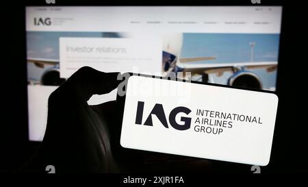 Stuttgart, Allemagne, 11-17-2023 : personne tenant un téléphone portable avec le logo d'International Consolidated Airlines Group sa (IAG) devant l'entreprise Banque D'Images