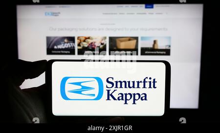 Stuttgart, Allemagne, 11-16-2023 : personne tenant un téléphone portable avec le logo de la société d'emballage irlandaise Smurfit Kappa Group plc devant la page Web de l'entreprise. Banque D'Images