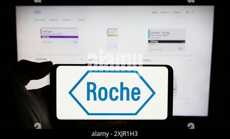 Stuttgart, Allemagne, 11-16-2023 : personne tenant un téléphone portable avec le logo de la société suisse de soins de santé Roche Holding AG devant la page web de l'entreprise. Banque D'Images