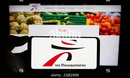 Stuttgart, Allemagne, 12 août 2023 : personne tenant un téléphone portable avec le logo de la société française ITM entreprises S.A. (les Mousquetaires) devant la page web. Banque D'Images