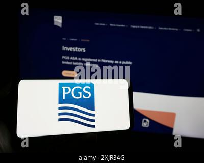 Stuttgart, Allemagne, 12-15-2023 : personne tenant un téléphone portable avec le logo de la société norvégienne de services pétroliers PGS ASA en face de la page Web de l'entreprise. Mise au point Banque D'Images