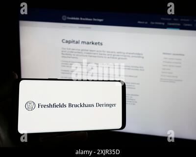 Stuttgart, Allemagne, 12-17-2023 : personne tenant un smartphone avec le logo du cabinet d'avocats britannique Freshfields Bruckhaus Deringer LLP devant le site Web. Mise au point Banque D'Images