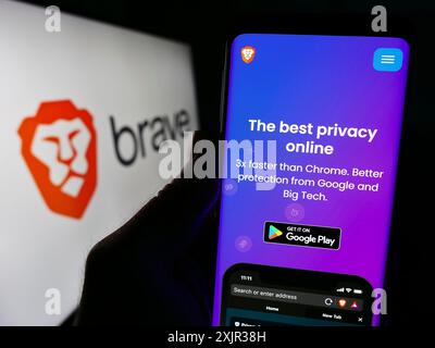 Stuttgart, Allemagne, 12-18-2023 : personne tenant un smartphone avec le site Web de la société américaine de navigateur Web Brave Software Inc devant le logo de l'entreprise. Mise au point Banque D'Images