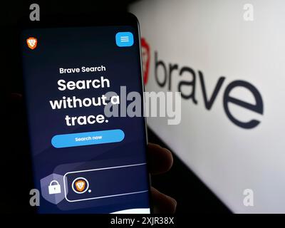 Stuttgart, Allemagne, 12-18-2023 : personne tenant un téléphone portable avec la page Web de la société américaine de navigateur Web Brave Software Inc devant le logo de l'entreprise. Mise au point Banque D'Images