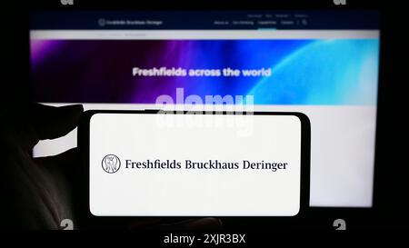 Stuttgart, Allemagne, 12-17-2023 : personne tenant un téléphone portable avec le logo du cabinet d'avocats britannique Freshfields Bruckhaus Deringer LLP devant l'entreprise Banque D'Images