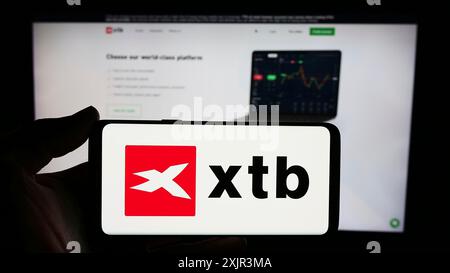 Stuttgart, Allemagne, 12-22-2023 : personne tenant un smartphone avec le logo de la société polonaise de courtage d'investissement XTB S.A. en face du site. Concentrez-vous sur le téléphone Banque D'Images