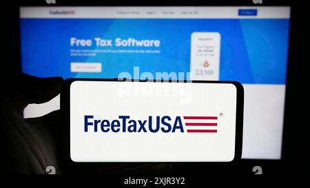 Stuttgart, Allemagne, 12-28-2023, une personne tenant un téléphone portable avec le logo de la société américaine de logiciels fiscaux en ligne FreeTaxUSA en face de la page Web de l'entreprise. Mise au point Banque D'Images