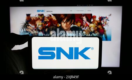 Stuttgart, Allemagne, 02-06-2024 : personne tenant un téléphone portable avec le logo de la société japonaise de jeux vidéo SNK Corporation en face de la page Web de l'entreprise. Banque D'Images