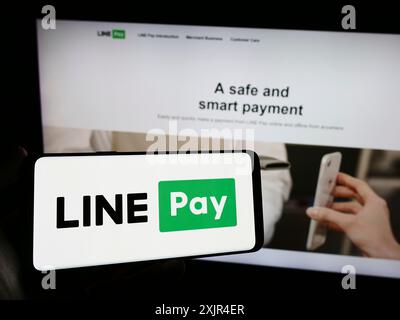 Stuttgart, Allemagne, 02-11-2024 : personne tenant un téléphone portable avec le logo de la société de paiements thaïlandais LIGNE payer en face de la page Web d'affaires. Concentrez-vous sur le téléphone Banque D'Images