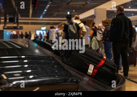 Personnes attendant leur valise sur le tapis roulant à bagages dans la zone de récupération des bagages à l'aéroport Banque D'Images