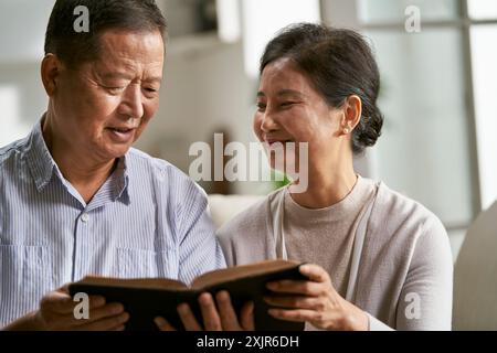 heureux couple asiatique senior assis sur le canapé de la famille à la maison lisant la bible ensemble Banque D'Images