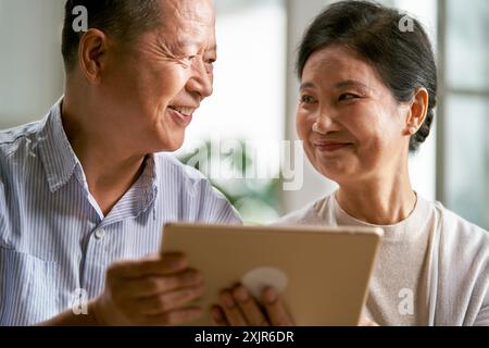 heureux couple asiatique senior assis sur le canapé à la maison en utilisant la tablette numérique ensemble Banque D'Images