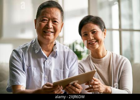heureux couple asiatique senior assis sur le canapé à la maison en utilisant la tablette numérique ensemble Banque D'Images