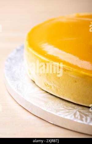 Un cheesecake à la mangue magnifiquement glacé garni d'une cuillère de purée de mangue et de feuilles de menthe fraîche. Le gâteau est présenté sur une planche à gâteau argentée Banque D'Images