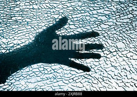 Silhouette d'une main derrière une surface de verre brisée, créant un effet visuel dramatique et abstrait. Banque D'Images