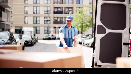 Le courrier efficace : un portrait d'un livreur heureux poussant des colis contre une fourgonnette dans un service de distribution Banque D'Images