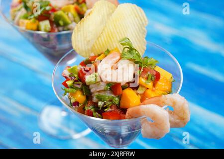 Salade de ceviche avec crevettes, mangue et avocat dans un bol en verre sur fond bleu. Cuisine latino-américaine. Délicieux ceviche de crevettes fraîchement préparées. Crevette ma Banque D'Images