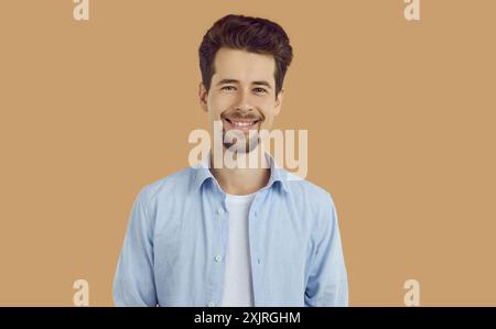 Portrait d'heureux brun souriant gars en chemise bleue sur fond beige regardant la caméra. Banque D'Images