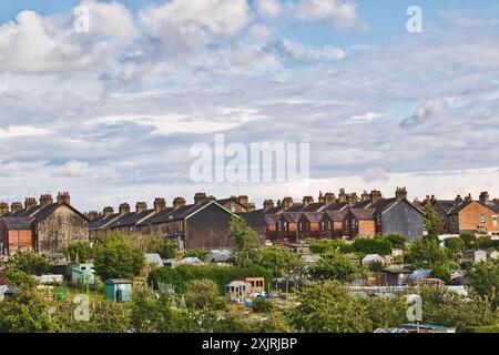 Une rangée de maisons mitoyennes britanniques traditionnelles avec des cheminées, vues de loin avec des jardins d'allotissement au premier plan sous un ciel partiellement nuageux. Banque D'Images