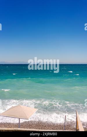 Image montrant une vue panoramique d'une mer turquoise avec des vagues douces sous un ciel bleu clair. Un parasol beige est au premier plan. Concept de Relax Banque D'Images