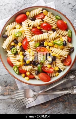 Salade de macaronis mexicains végétariens avec haricots noirs, maïs, tomate, oignon et jalapeno gros plan dans une assiette sur la table. Vue verticale de dessus depuis abo Banque D'Images