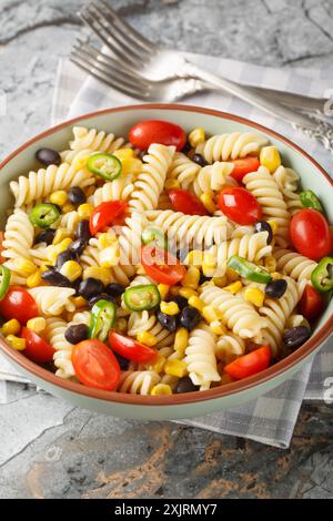 Salade de pâtes fraîches fusilli, haricots noirs, tomate et maïs gros plan dans une assiette sur la table. Vertical Banque D'Images