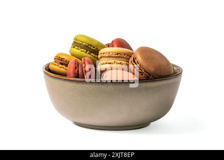 Gros plan d'un bol en céramique rempli de macarons colorés, chacun avec une garniture délicate, sur fond blanc. Le bol est un wi brun pâle Banque D'Images