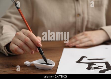 Calligraphie. Femme trempant le pinceau dans le puits d'encre à la table en bois, gros plan. Pratiquer l'écriture des hiéroglyphes chinois Banque D'Images