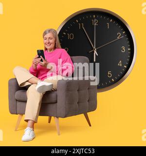 Femme mature avec smartphone assis dans un fauteuil près de la grande horloge sur fond orange Banque D'Images