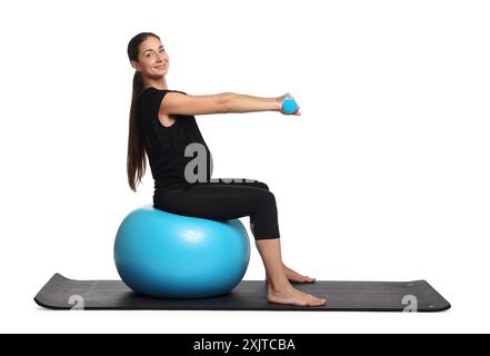 Belle femme enceinte avec des haltères faisant des exercices sur fitball sur fond blanc Banque D'Images