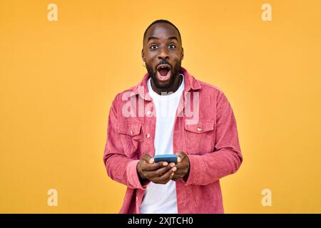 Homme africain excité tenant le téléphone surpris avec la victoire de pari isolé sur jaune. Banque D'Images