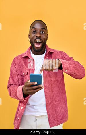 Homme africain excité tenant le téléphone surpris avec la victoire de pari isolé sur jaune. Banque D'Images