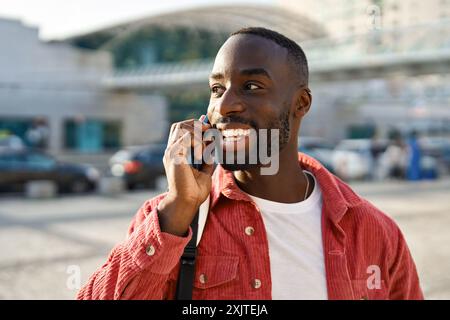 Heureux jeune homme africain debout dans la ville parlant sur le téléphone portable. Banque D'Images