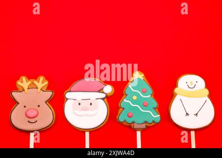 Biscuits glacés sur le thème de Noël en forme de renne, Père Noël, arbre de Noël et bonhomme de neige sur fond rouge Banque D'Images