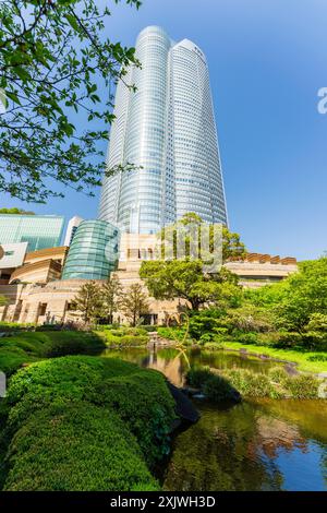 La tour Mori, avec le bâtiment d'entrée du musée d'art Mori en face, surplombant le spectateur dans le ciel bleu ensoleillé. Jardin au premier plan. Roppongi Hills. Banque D'Images