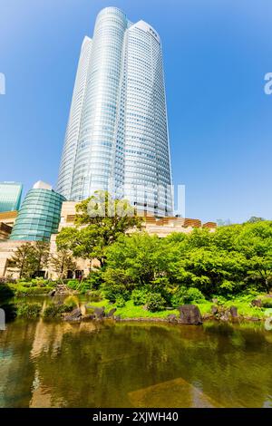 La tour Mori, avec le bâtiment d'entrée du musée d'art Mori en face, surplombant le spectateur dans le ciel bleu ensoleillé. Jardin au premier plan. Roppongi Hills. Banque D'Images