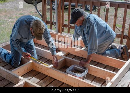 Deux hommes seniors dans leurs 80 ans à genoux travaillant, construisant un cadre en bois pour un mur extérieur pour une petite maison, USA. Banque D'Images