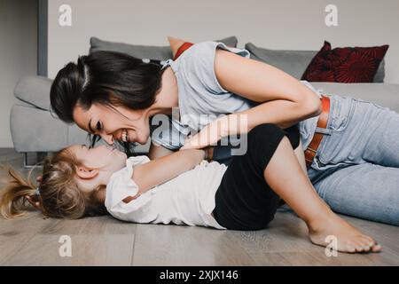 Mère et fille partagent un moment heureux en jouant sur le sol confortable de leur salon, créant une atmosphère joyeuse d'amour et de convivialité Banque D'Images