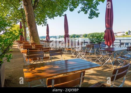 Un jardin de bière vide avec des tables et des chaises à l'ombre des arbres par une journée ensoleillée, avec une vue sur le Rhin à Neuwied, Allemagne. Banque D'Images