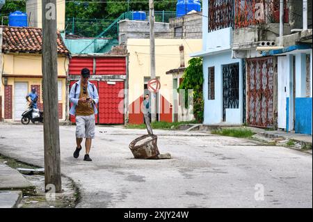 Un cubain marche par un trou d'homme sans couvercle dans une rue de ville. Santa Clara, Villa Clara, Cuba, 2024 Banque D'Images